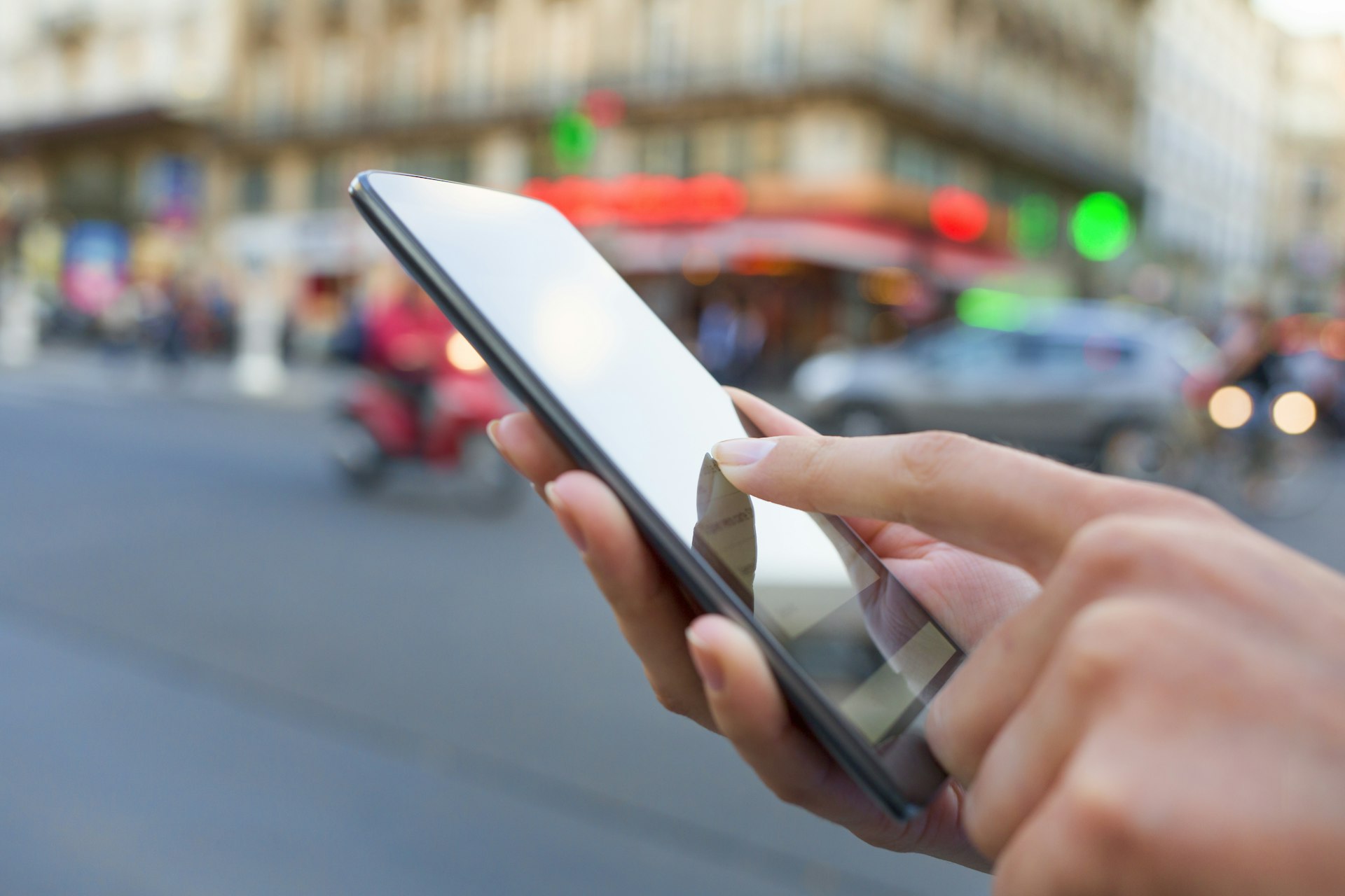 A hand holding a smart phone at a busy street intersection in Paris