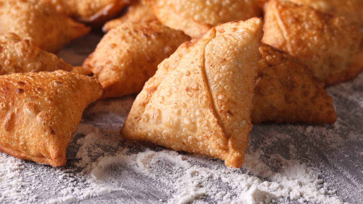 Close-up of a pile of fried samosas on a floured table.
