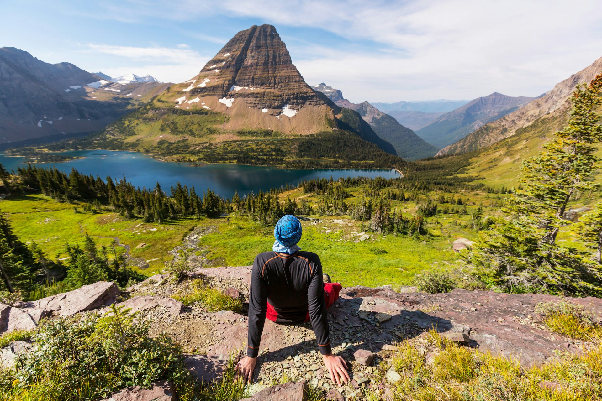 A hiker sits on a rock looking out at a stunning landscape of peaks and lakes