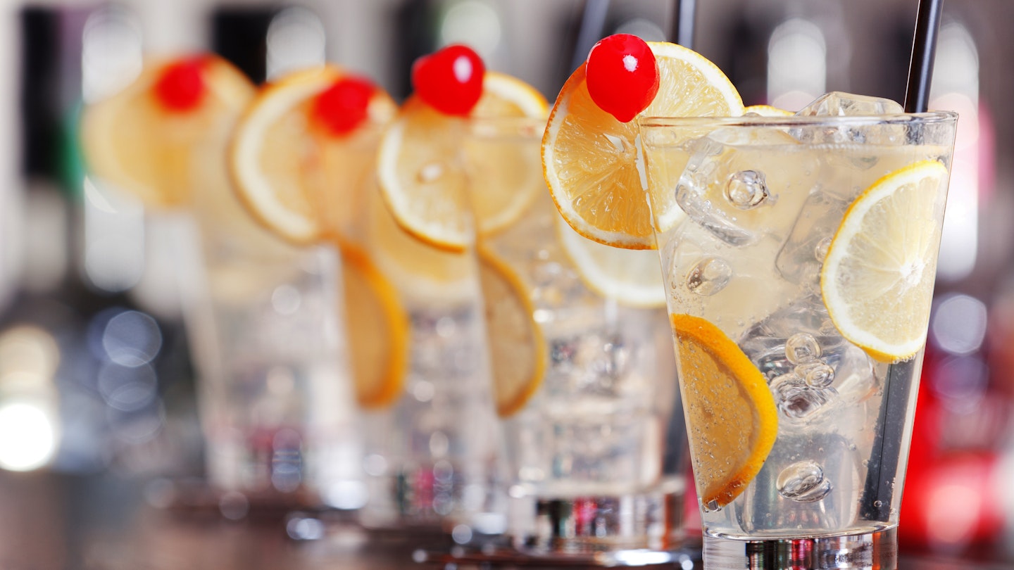 Four Tom Collins alcoholic cocktails on a bar.