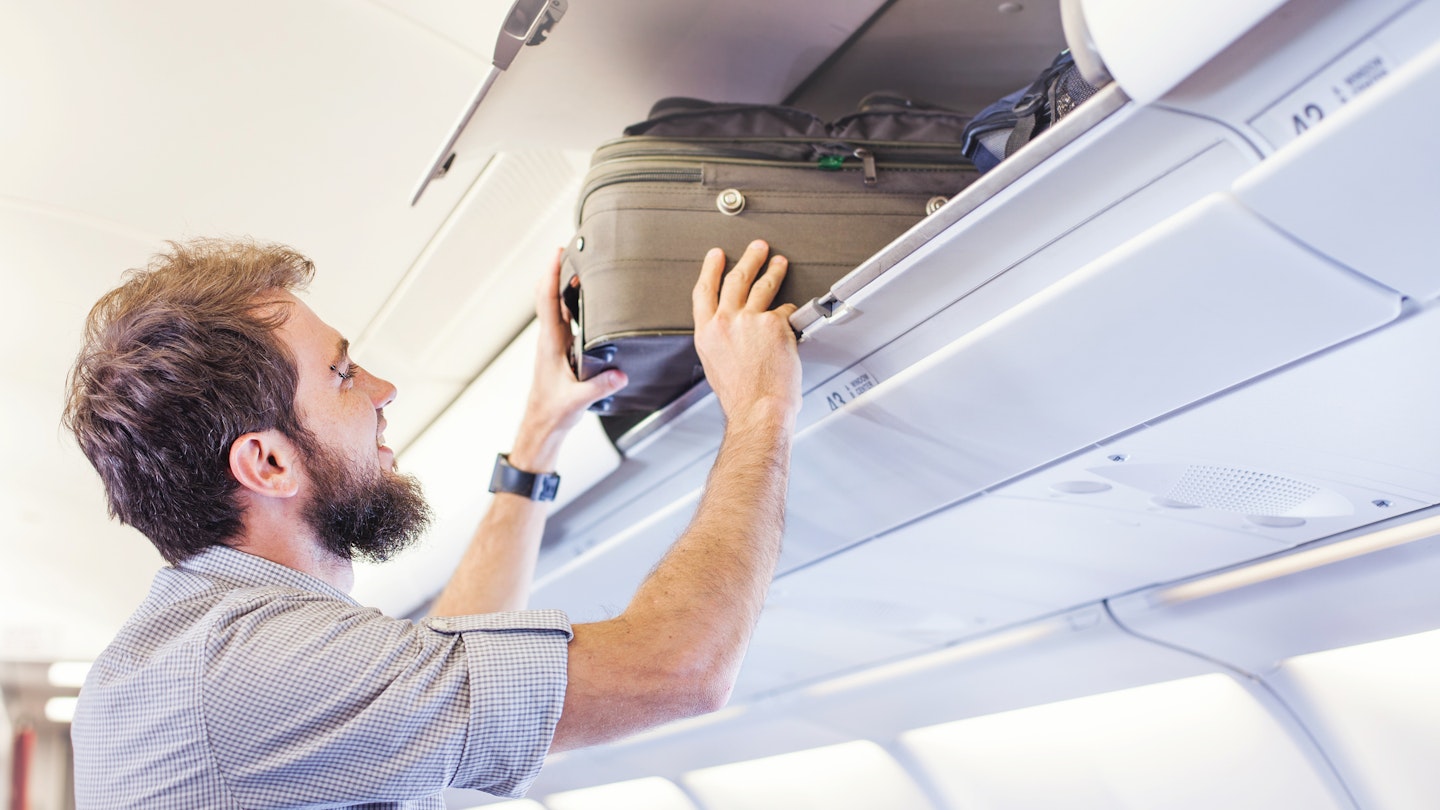 Man putting luggage in the hand-luggage compartment of an airplane.