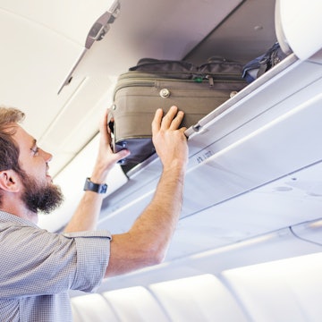 Man putting luggage in the hand-luggage compartment of an airplane.