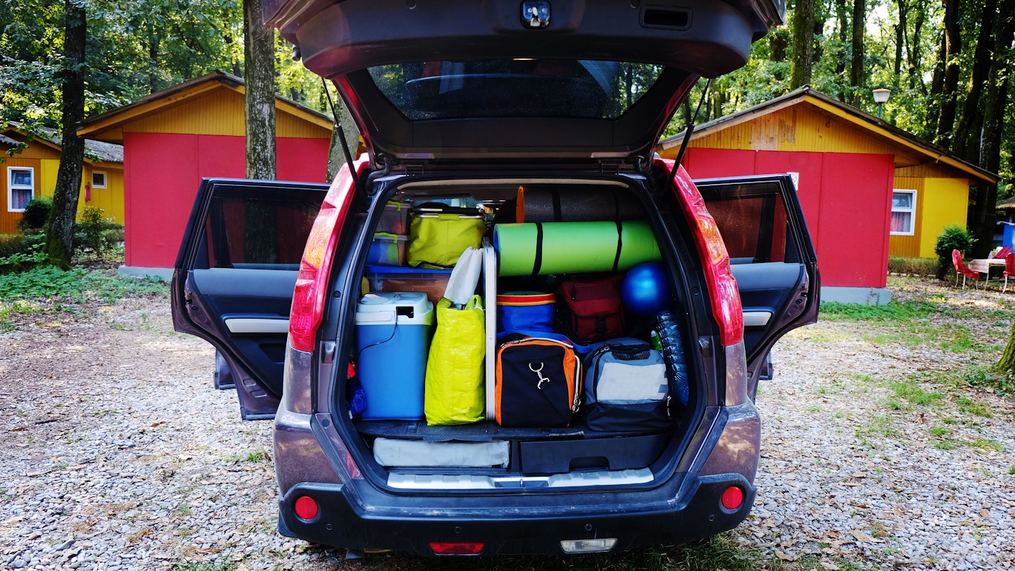 Camping luggage tightly packed into a car trunk in a forest setting.