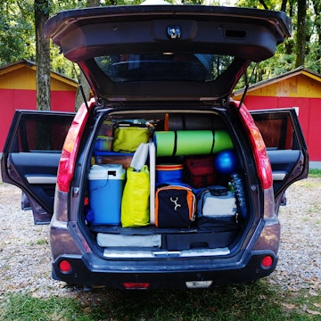 Camping luggage tightly packed into a car trunk in a forest setting.