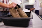 Man putting shoes into a tray at an airport security check.