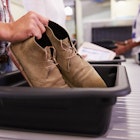 Man putting shoes into a tray at an airport security check.