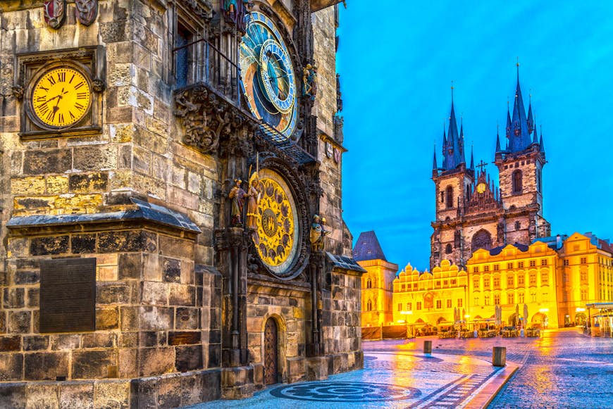 A damp city square in the evening with an ornate astronomical clock in gold and blue