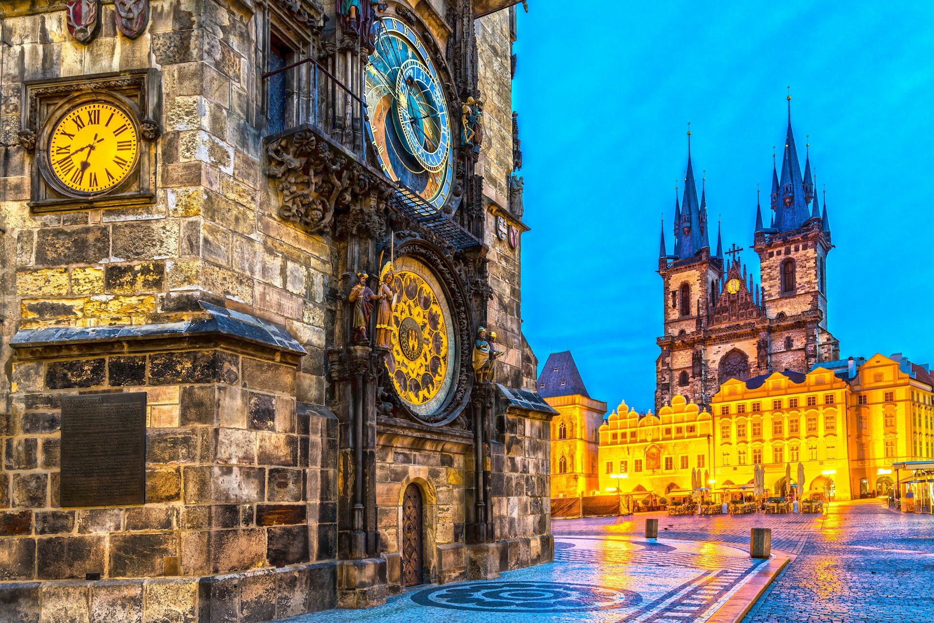 A damp city square in the evening with an ornate astronomical clock in gold and blue