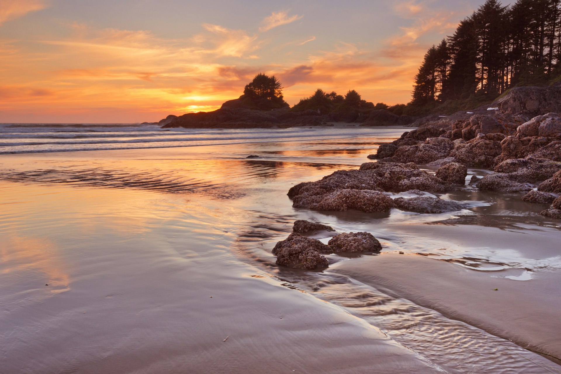 An orange-pink sunset bathes the beach at Cox Bay on Vancouver Island, Canada