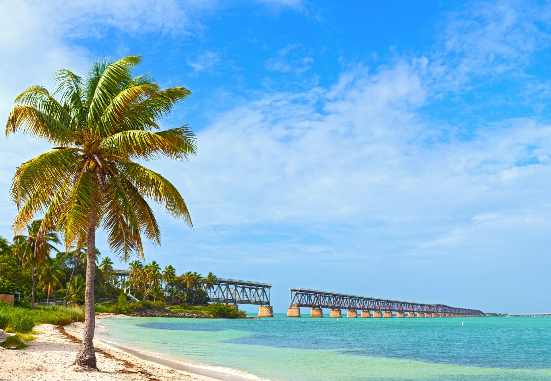 A tropical beach with a railroad bridge in the background