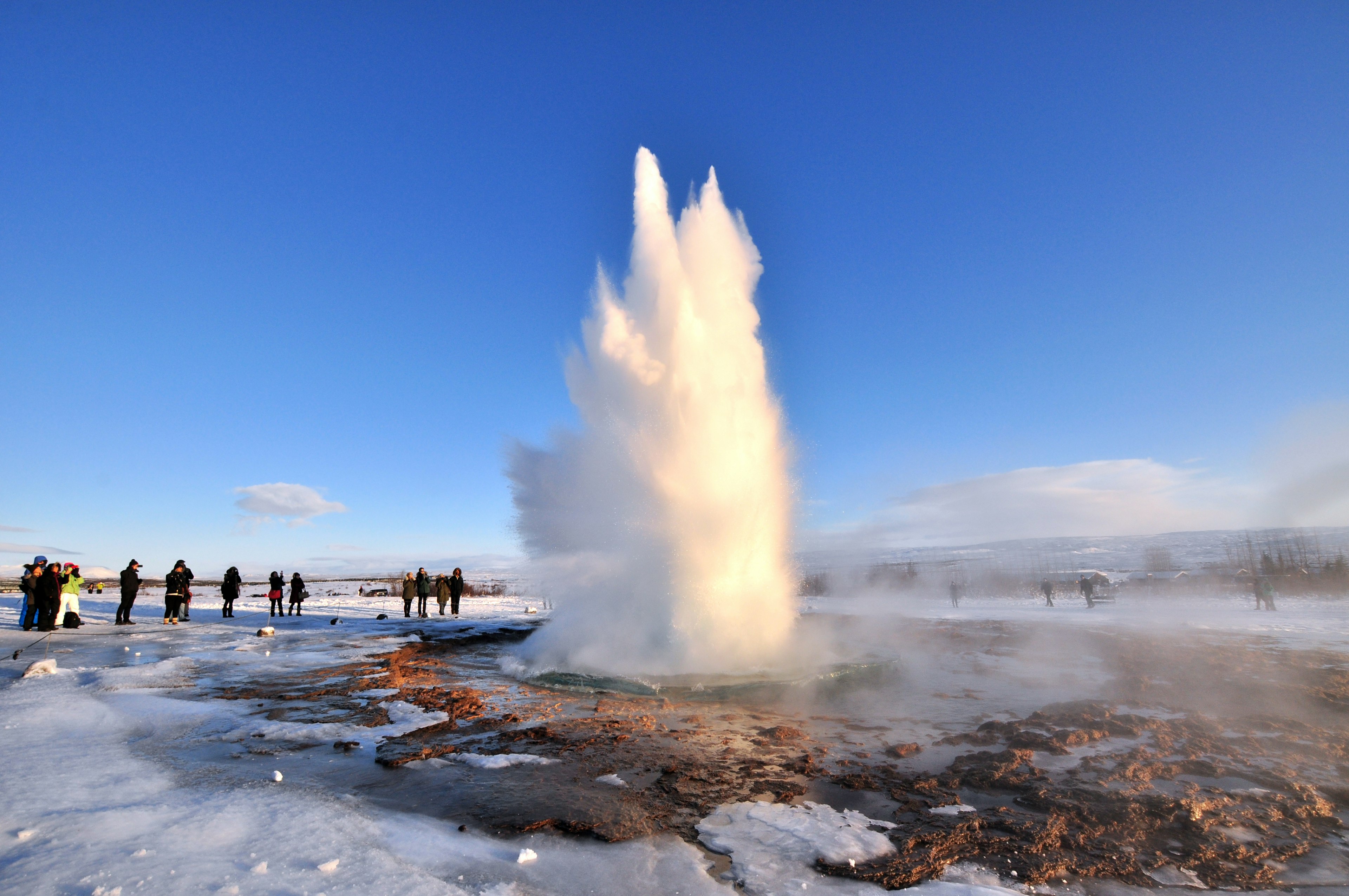 A group of people watch Stokkur geyser erupt on a sunny, wintry day.