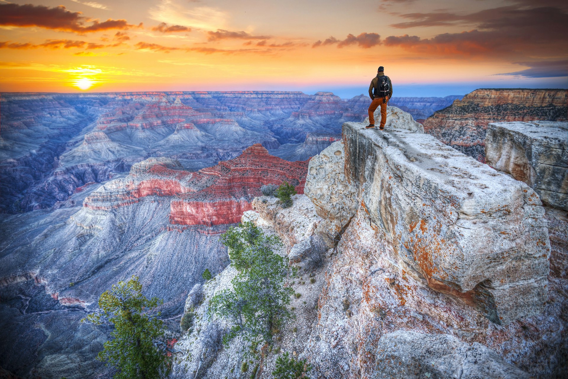 A man stands on the edge of a rock at the Grand Canyon at sunrise 