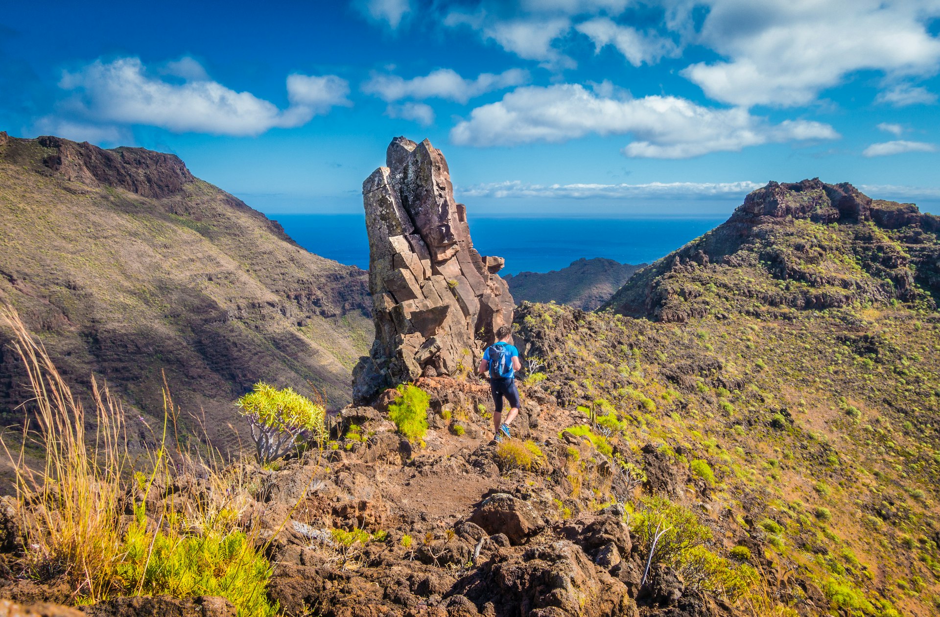 A hiker on a remote trail through rocky formations with the sea in the distance in the Canary Islands