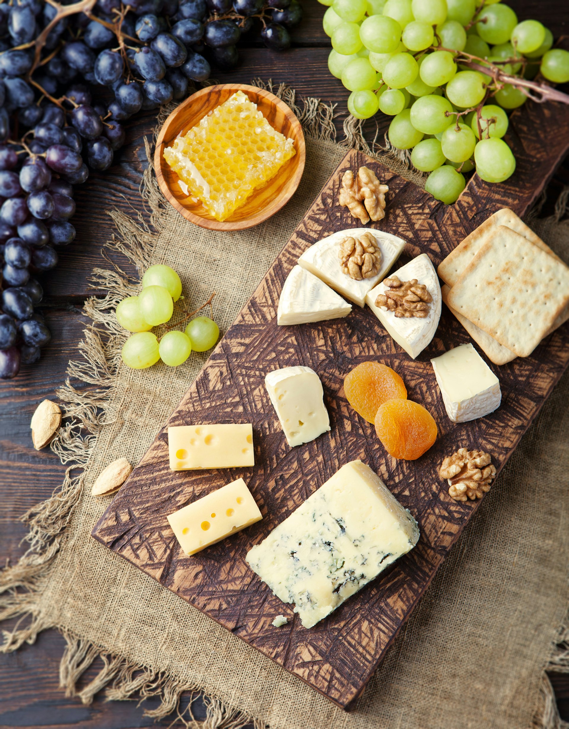 Assortment of cheese with honey, nuts and grape on a rustic cutting board wooden background toning