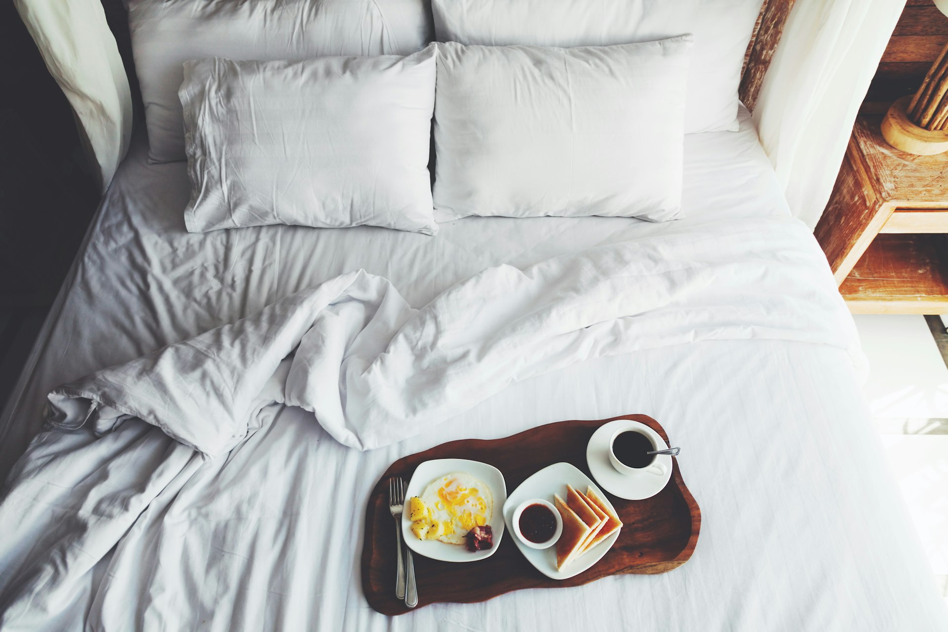 Breakfast on a tray in bed in hotel, white linen, wooden interior 