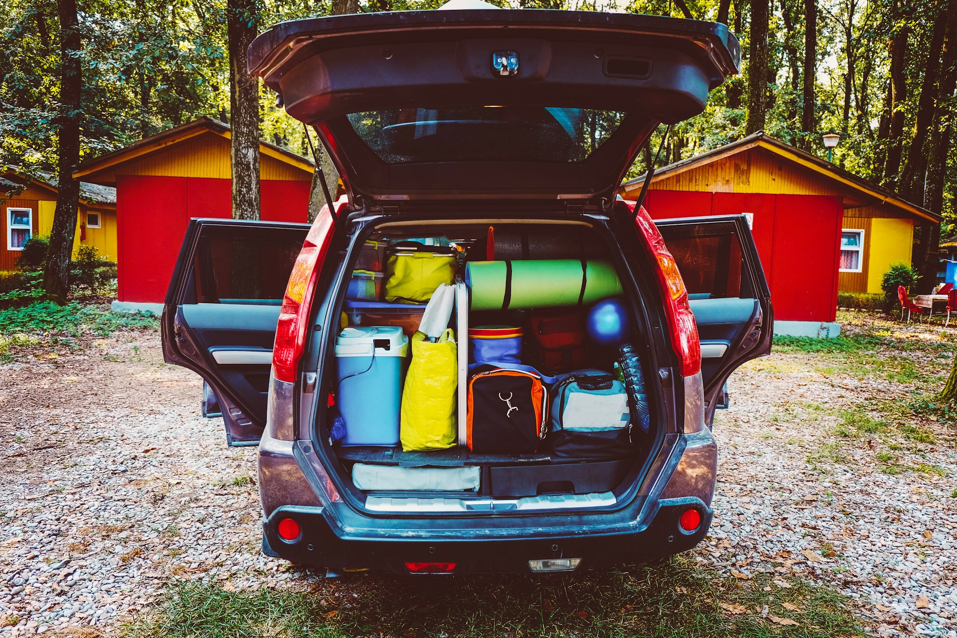 Camping luggage tightly packed into a car trunk in a forest setting. 