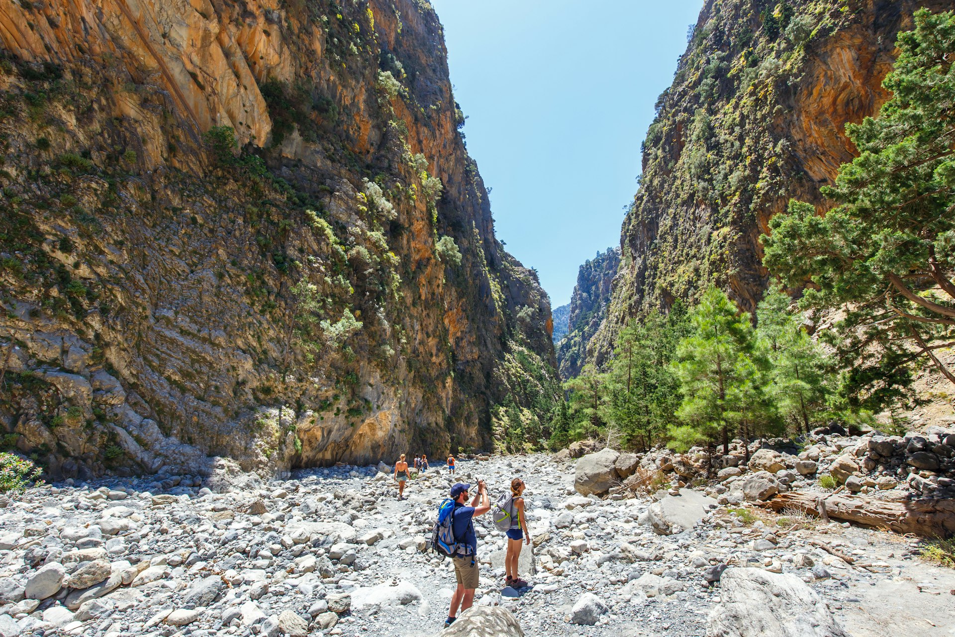 Tourists hike through Samaria Gorge in central Crete. The rocky walls of the gorge loom large in the background, making the hikers look very small.