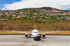 Passenger jet on the airport tarmac with Agua de Pena village in the background.