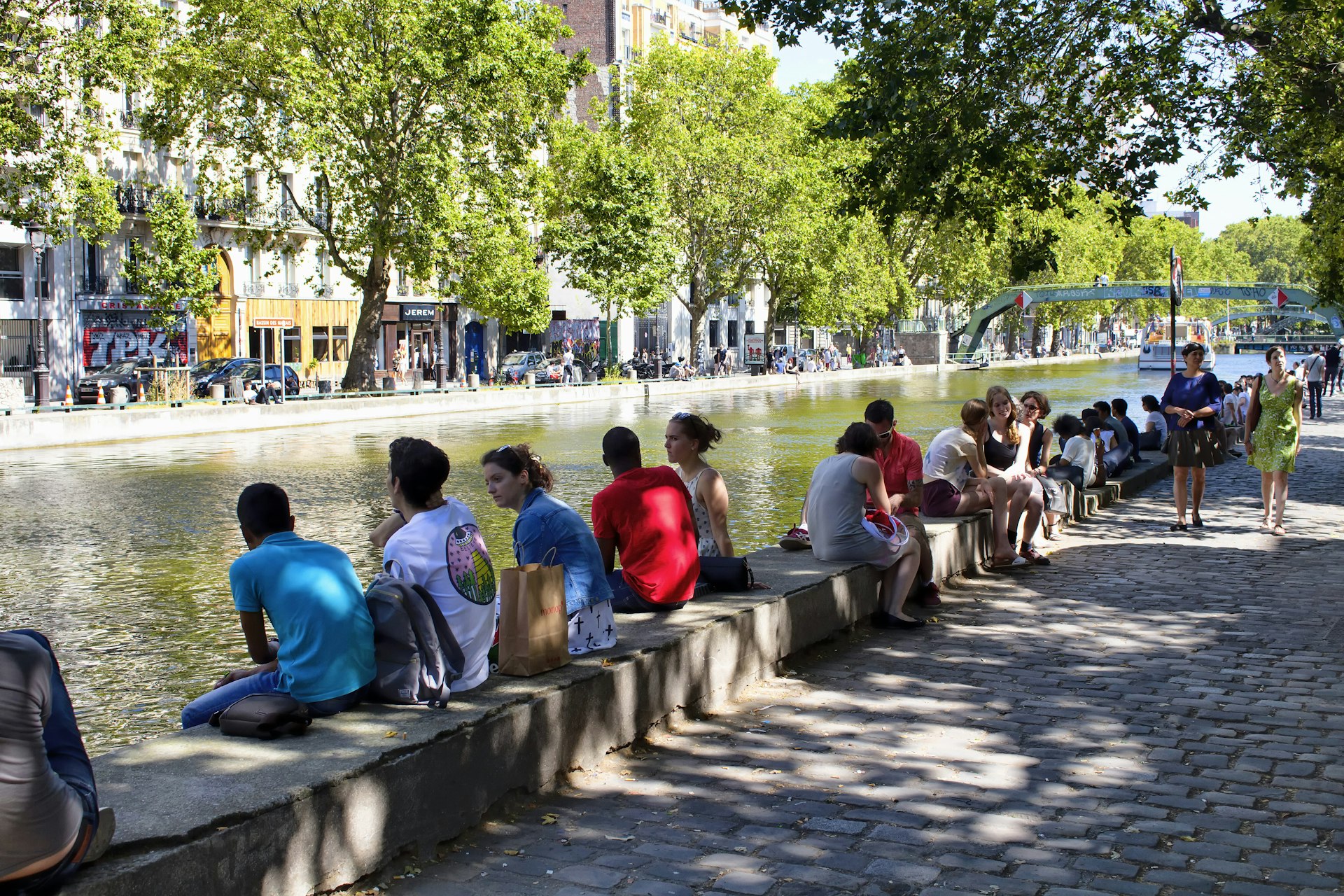 People hang out by Canal Saint Martin under trees in Paris