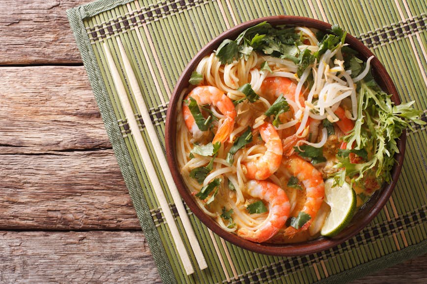 Malaysian laksa soup with shrimps, noodles and herbs in a bowl on the table