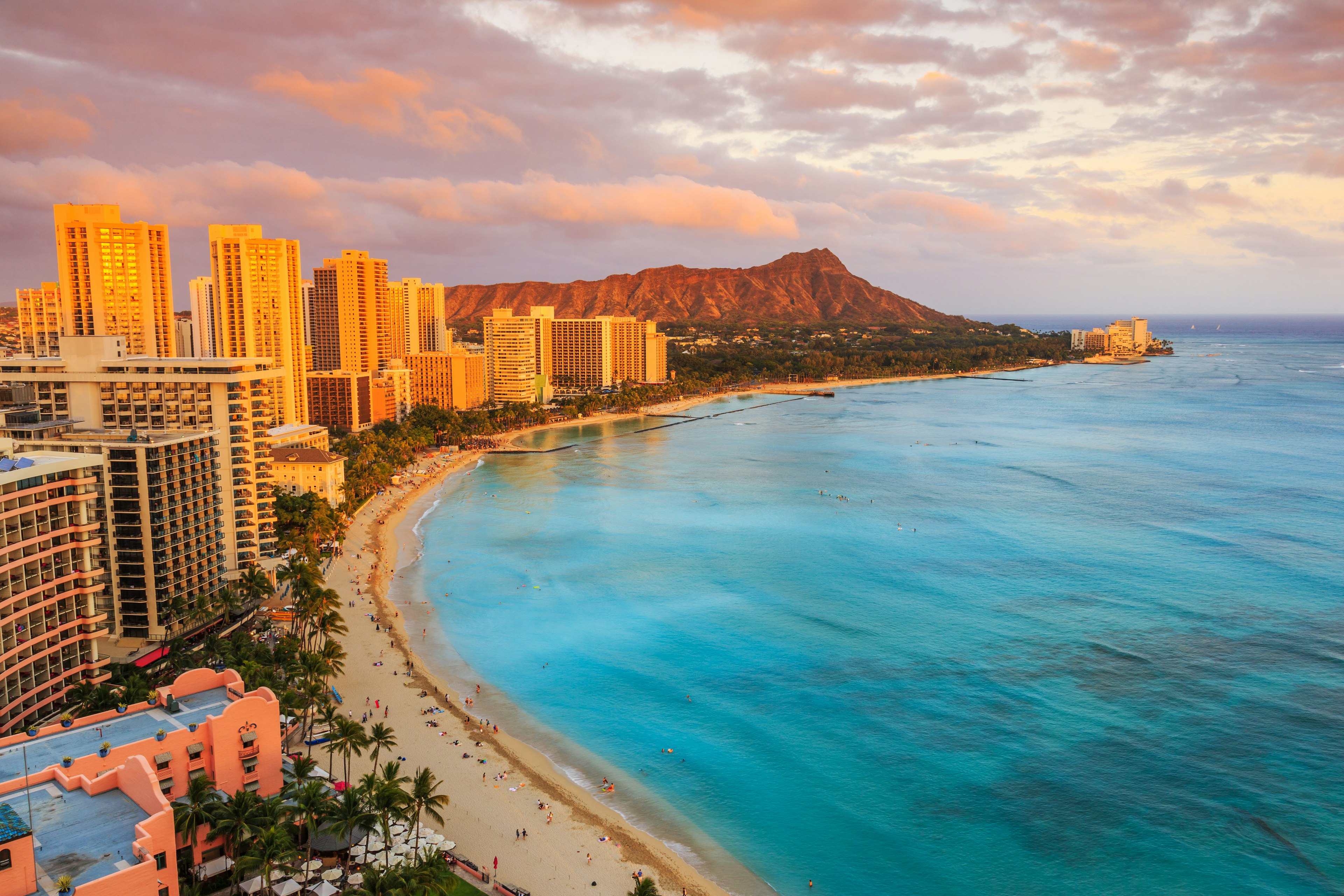 Rows of high-rise buildings back a curve of golden sand with a volcano peak in the distance