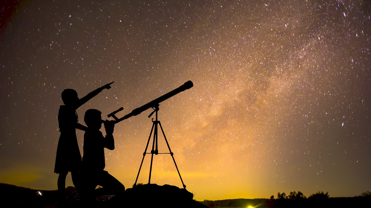 Silhouette of children looking through a telescope at the Milky Way galaxy.