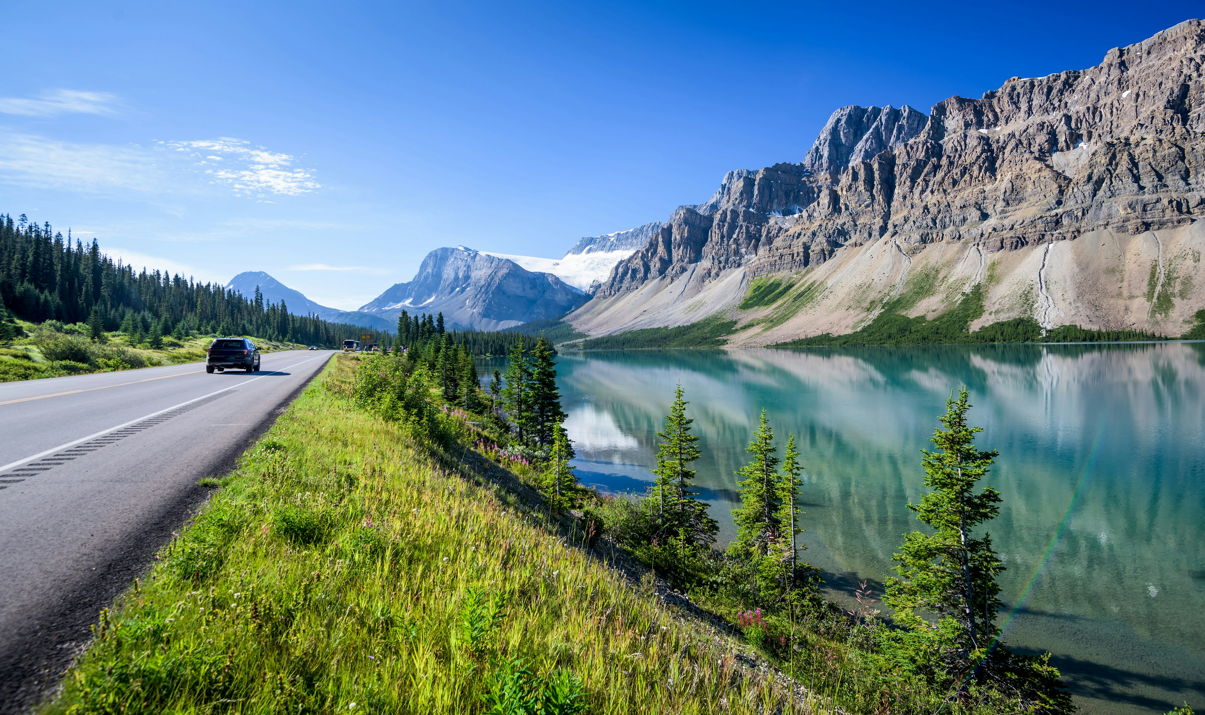 A road runs alongside a turquoise lake with large granite outcrops stretching into the distance