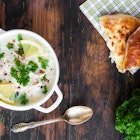 Avgolemono, chicken soup with egg-lemon sauce, rice and fresh parsley leaves in white bowl and freshly baked bread on wooden table. Top view.