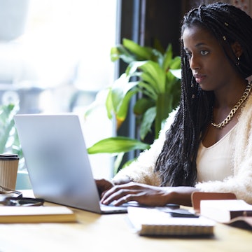 Afro American female using modern laptop computer in coffee shop.