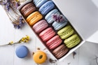 Colorful macaroons in a gift box with flowers on wooden table.