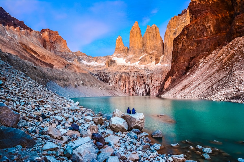 A couple sit on a rock at Laguna Torres and observe the famous three towers in dawn light.