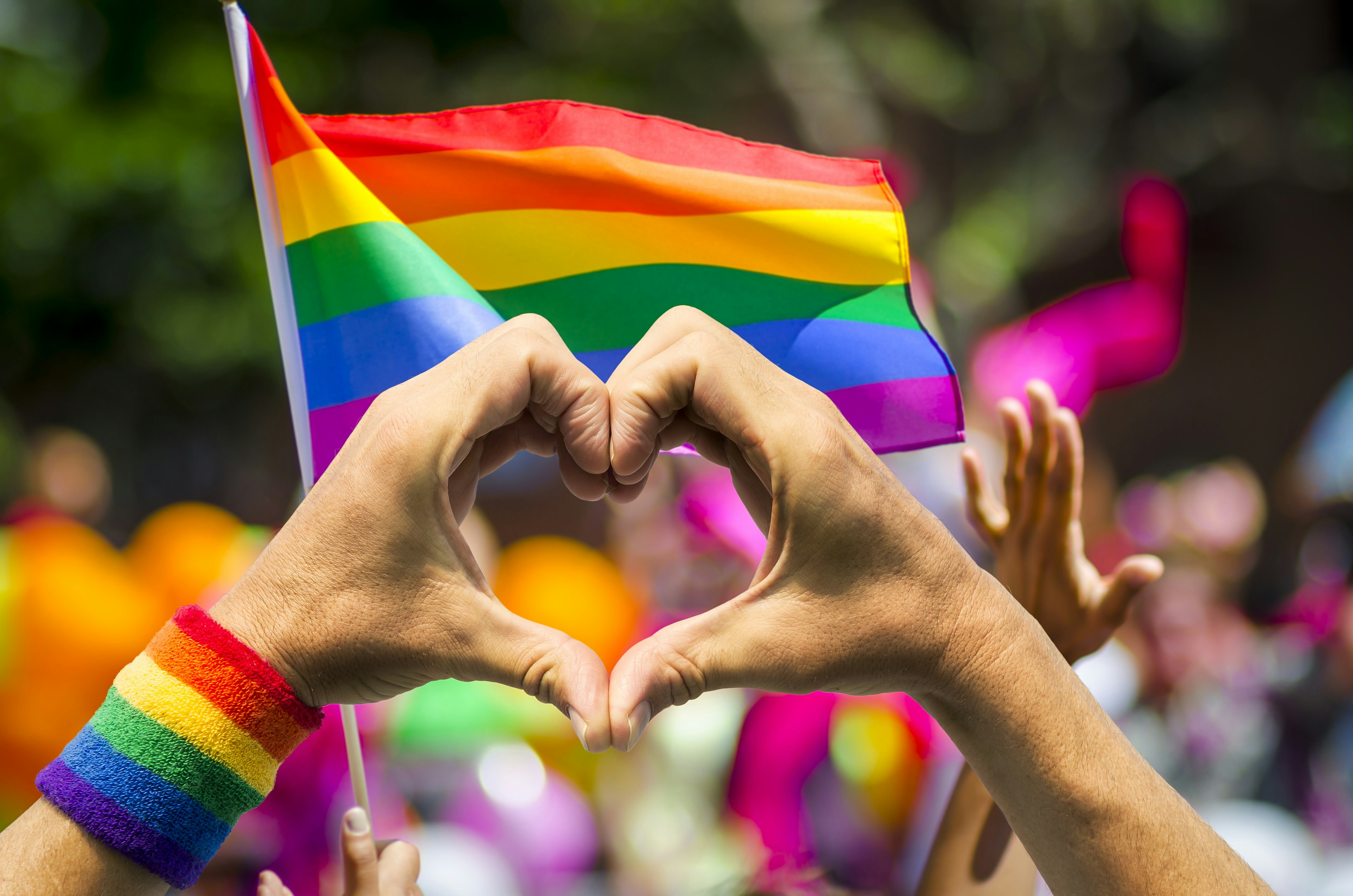 Supporting hands make a heart sign in front of a rainbow flag at a summer gay pride parade in New York.