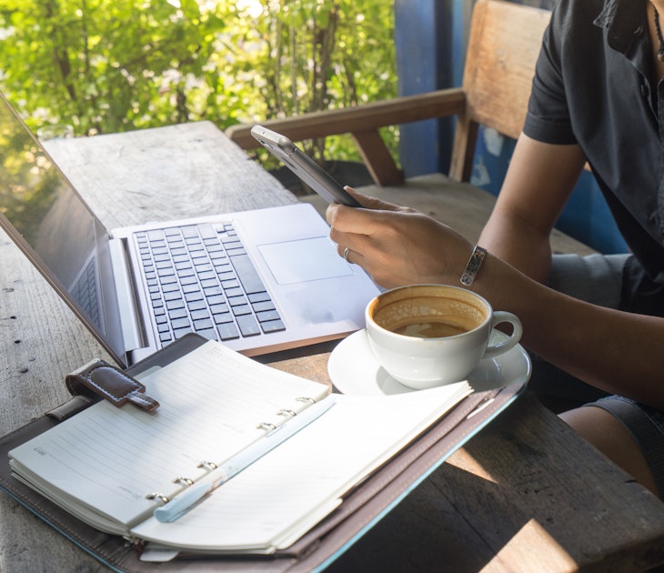 Asian man digital nomad sit and working on freelance project using portable computer, smartphone and making notes in the paper note.