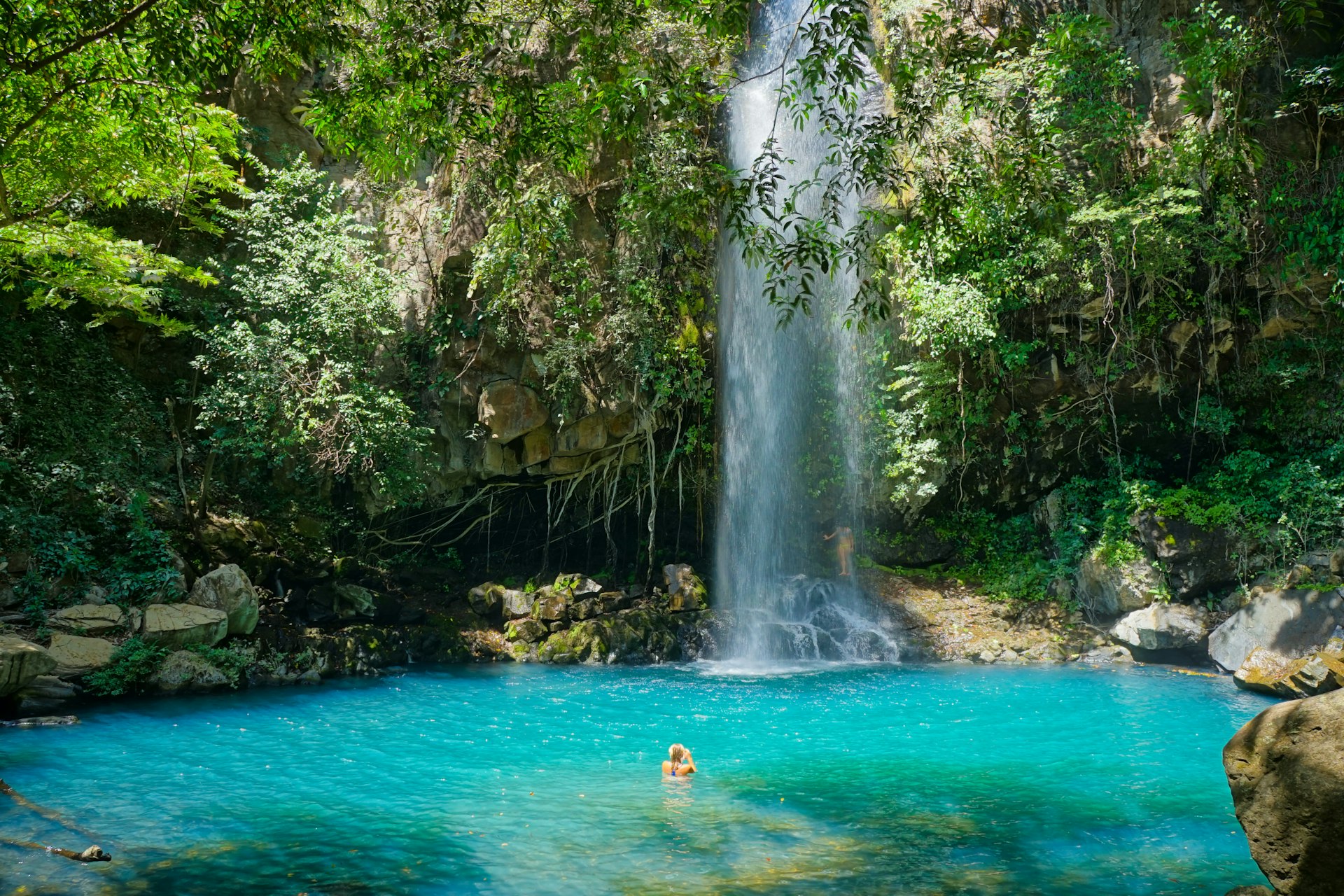 A person swims toward a waterfall at Rincón de la Vieja Volcano in Guanacaste Province