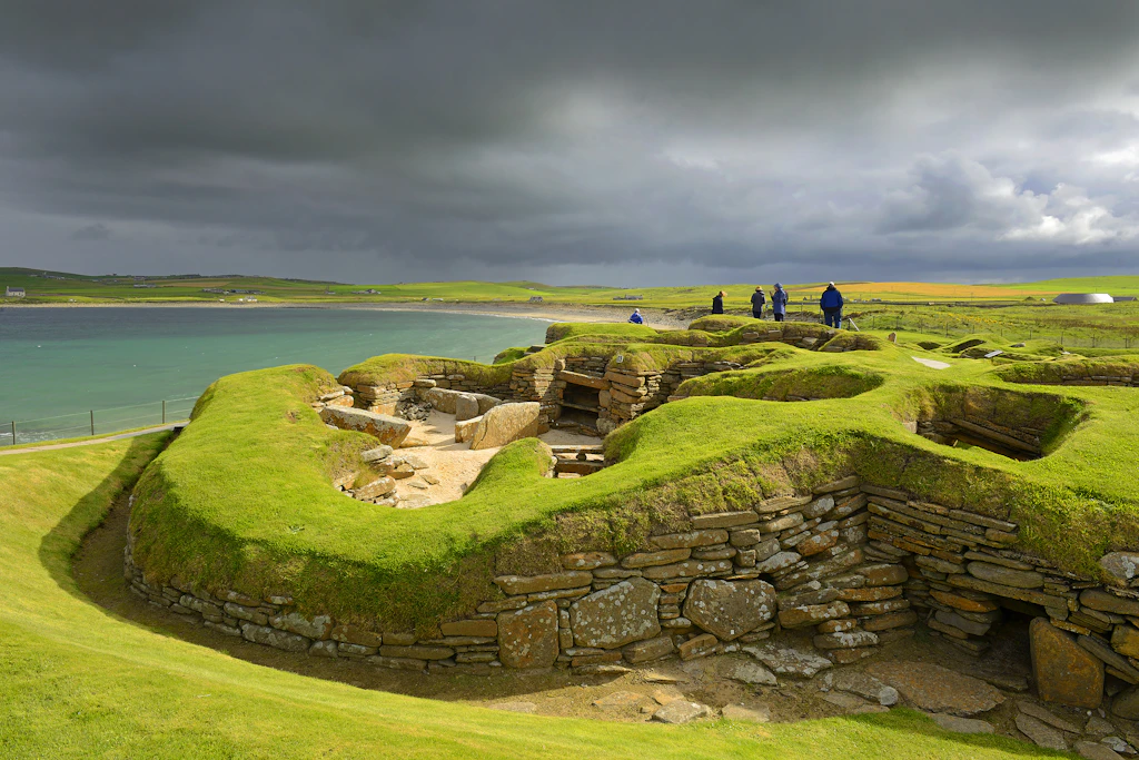 Skara Brae Prehistoric Village A series of stone houses built into green mounds of earth on the edge of an island with the grey sea churning nearby