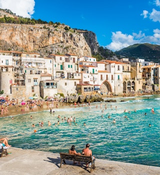 AUGUST 12, 2017: Visitors crowd the beach at Cefalu on a sunny day.