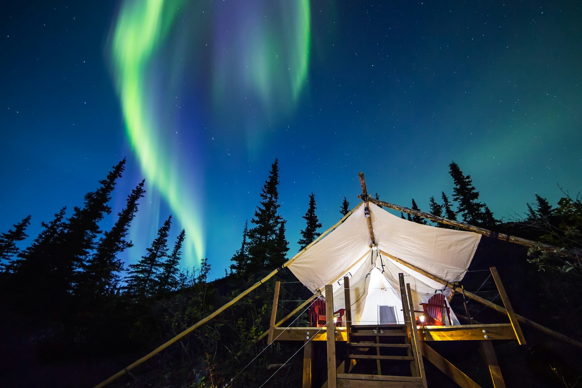 Aurora Borealis glowing green and pink over a large canvas luxury camping tent in Alaska