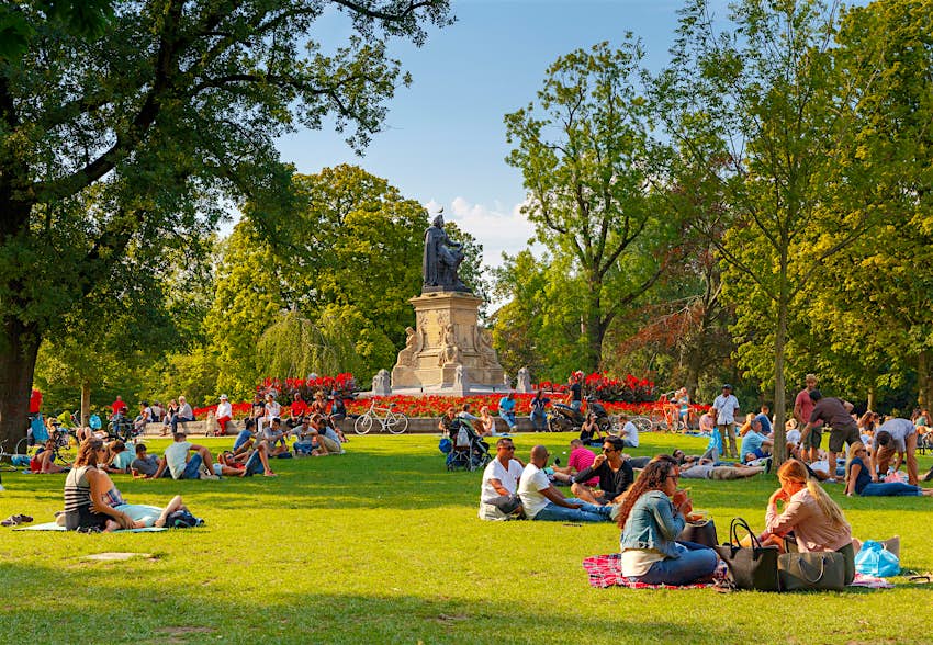 Μεγάλο πράσινο ανοιχτό πάρκο με μικρές ομάδες ανθρώπων κάθονταν έξω στον ήλιο