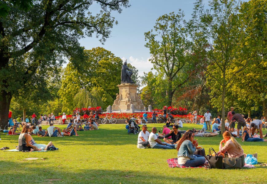 Stor grön öppen park med små grupper av människor satt ute i solskenet