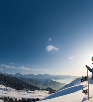 An image with a portrait of a female snowboarder wearing a helmet with a bright reflection in the glasses on the background of high snow-capped Alps in Grindelwald, Swiss