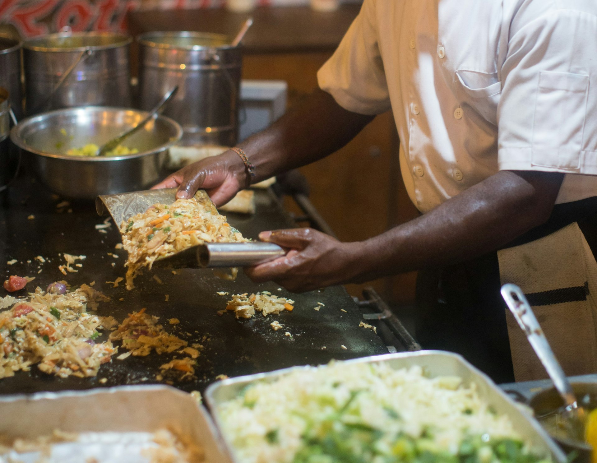 Kothu roti being made on a tabletop surface. The ingredients are being mixed together using two flat metallic utensils.