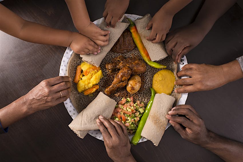 many hands reaching to take some injera with a variety of food