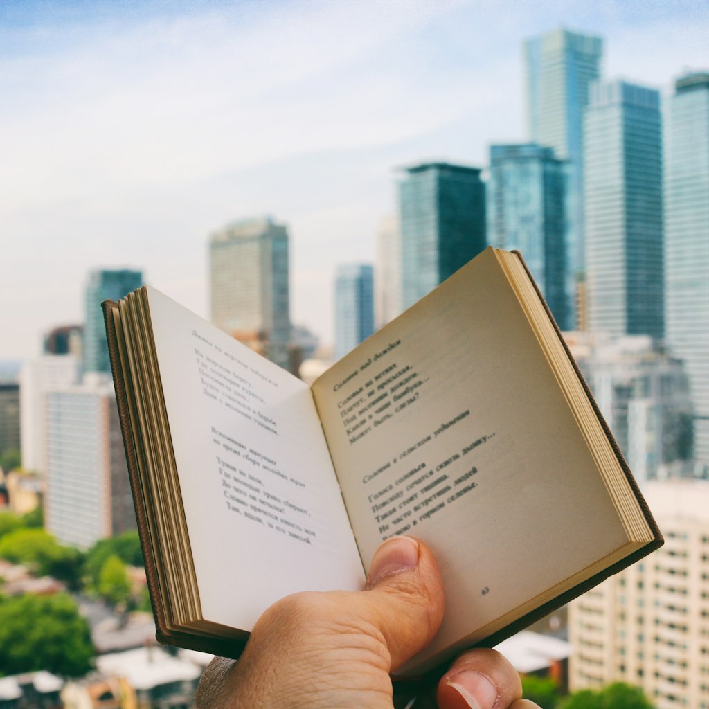 Holding the open book, enjoying reading poetry, while on the rooftop patio with the view of the city life in the background. Part of 'Reading The Book' Series. (Creative Brief - Digital Wellbeing)
