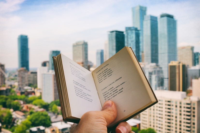 Holding the open book, enjoying reading poetry, while on the rooftop patio with the view of the city life in the background. Part of 'Reading The Book' Series. (Creative Brief - Digital Wellbeing)