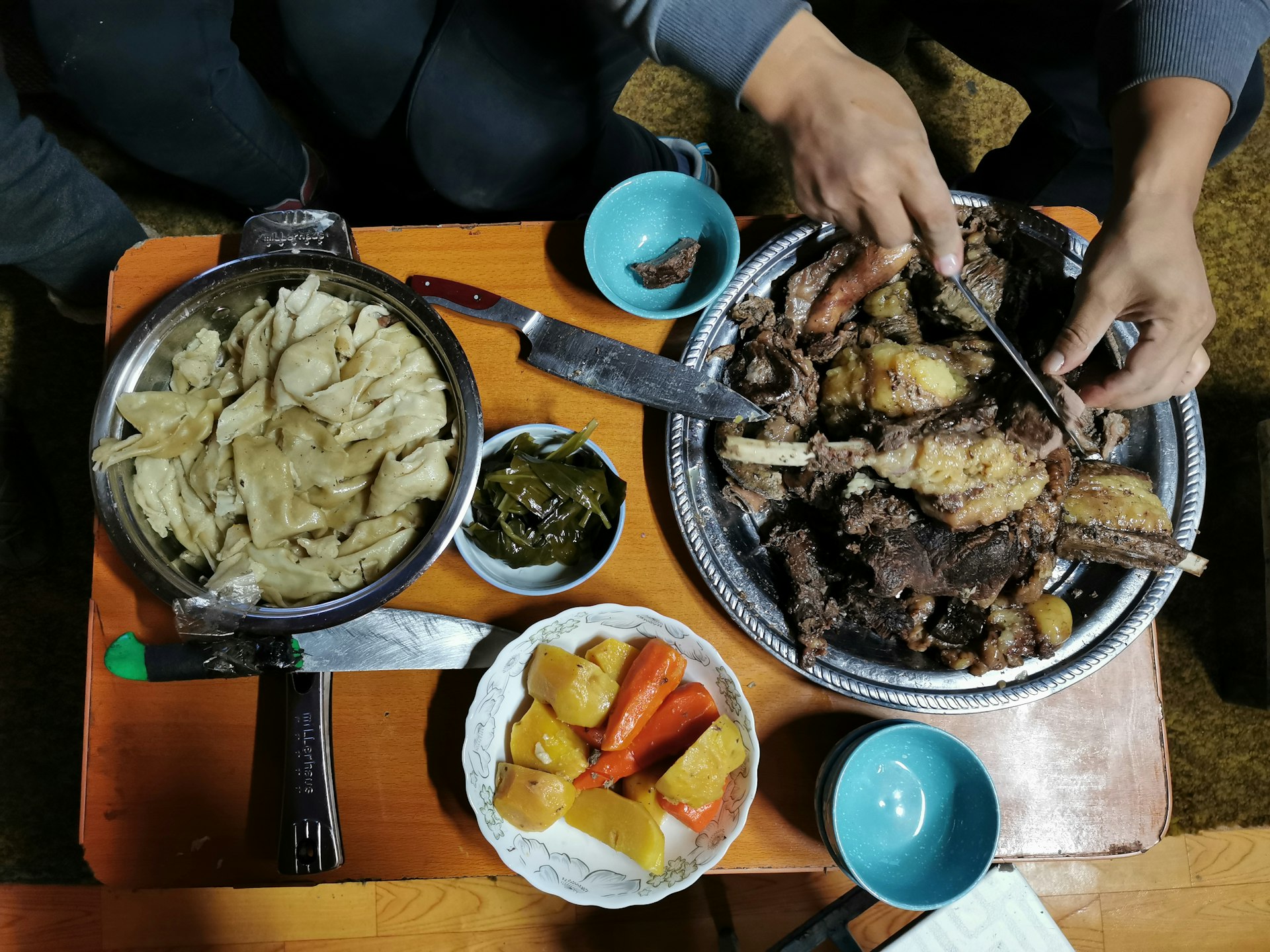 Four bowls of food on a small wooden table, including a bowl of greens and fried horse meat