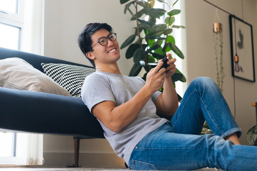 Cheerful young man playing video game, sitting on the floor at home during the day.