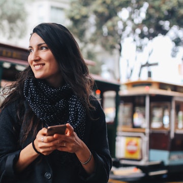 Young woman walking in downtown San Francisco, California. She is wearing casual clothing, sightseeing the old and beautiful San Francisco downtown area, texting on the smart phone.
