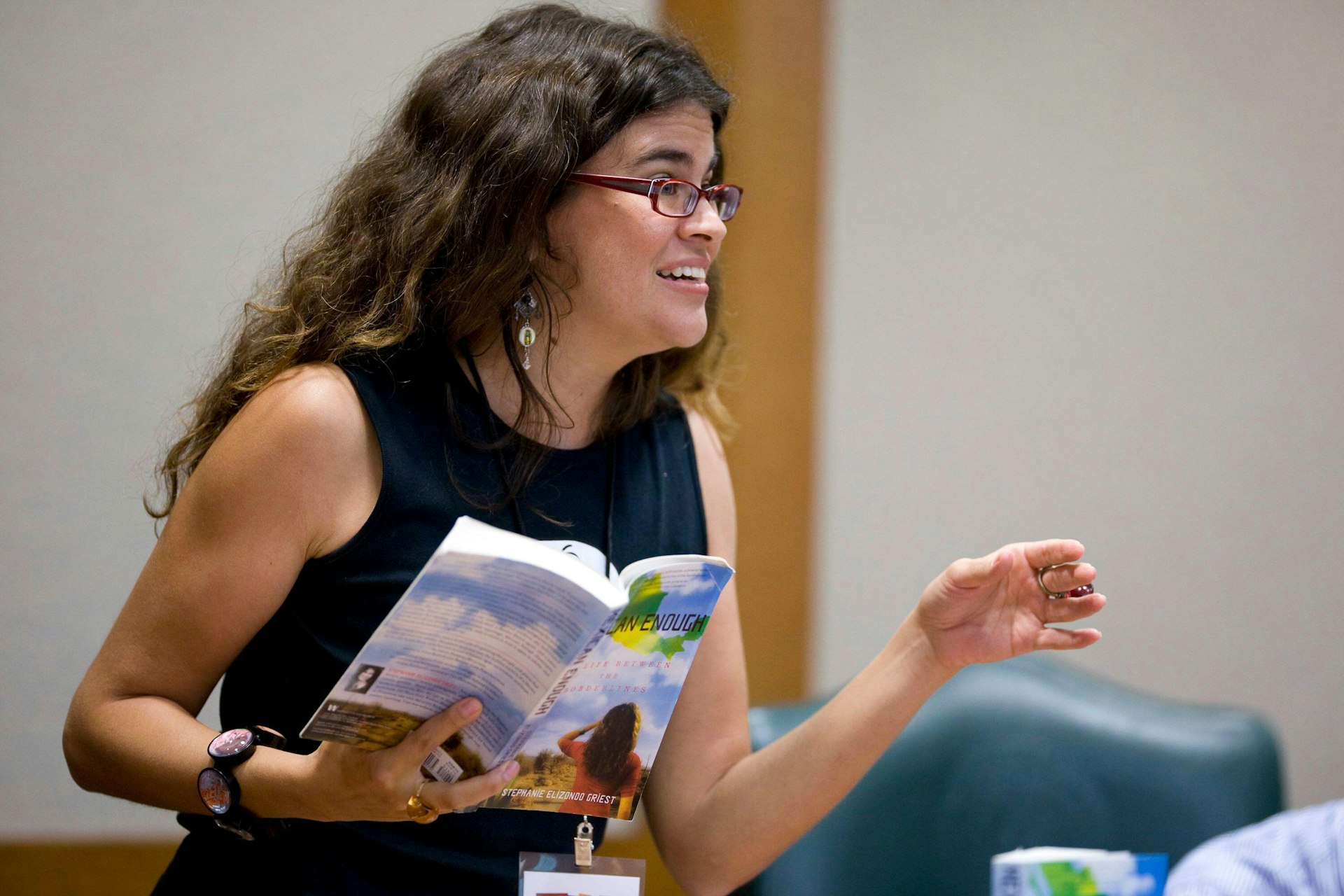 A woman, Stephanie Elizondo Griest, reads from a book in front of a crowd. 