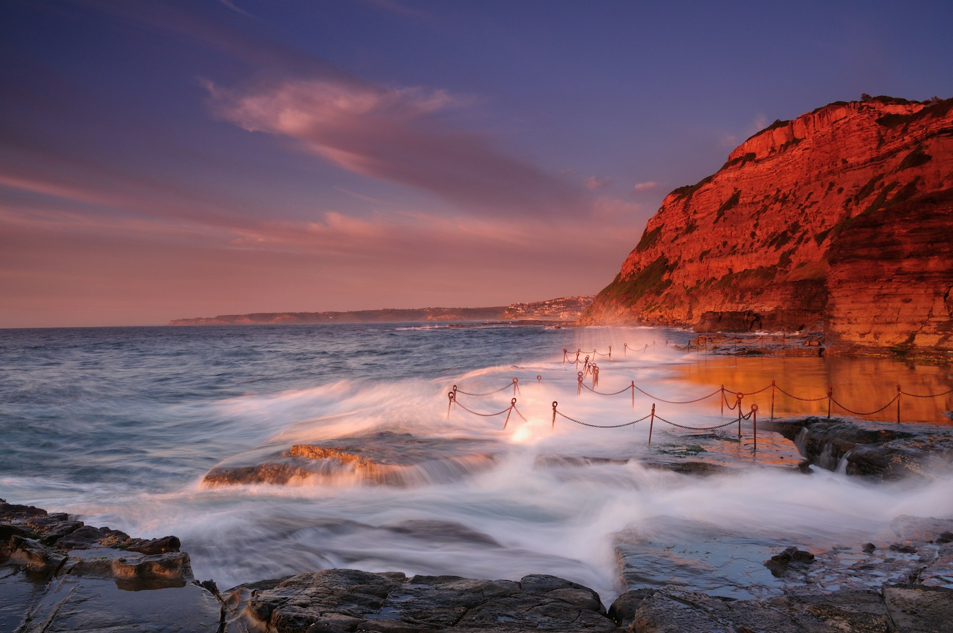 Ocean waves crash against jagged rocks at the Bogey Hole in Newcastle, at high tide.