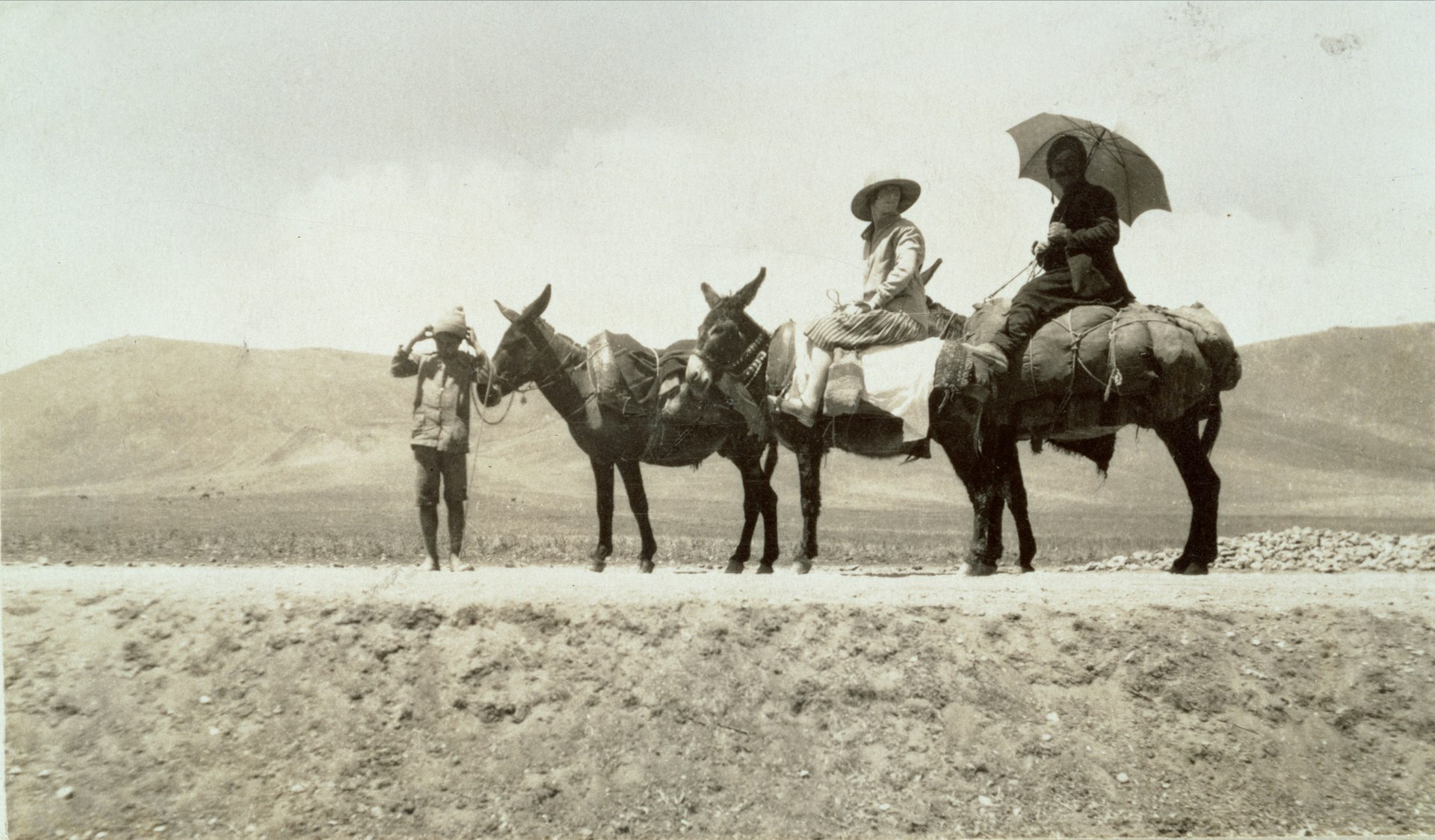 A woman rides a horse in the desert in an old photo. 